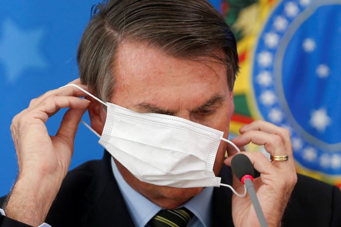 Brazil's President Jair Bolsonaro wearing a protective face masks reacts during a news conference to announce measures to curb the spread of the coronavirus disease (COVID-19) in Brasilia